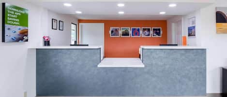 Un espace d’accueil avec un comptoir de réception gris, un présentoir blanc et un mur orné de tableaux.
