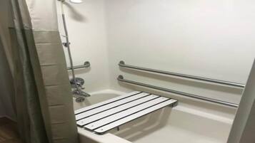 A shower area with a white bathtub, a handheld showerhead, and a safety grab bar.