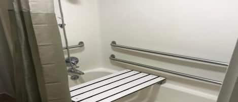 A shower area with a white bathtub, a handheld showerhead, and a safety grab bar.