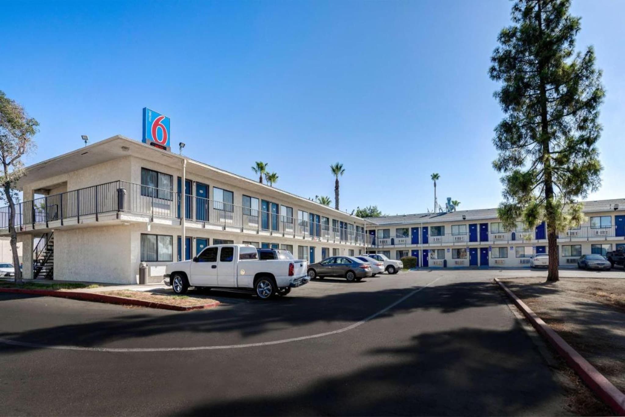 A motel with a row of rooms, a parking lot, and a clear blue sky.