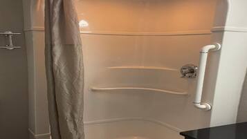 A corner shower with a curved door, a handrail, and a ceiling-mounted light fixture.