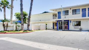 A two-story building with a flat roof, a balcony on the upper floor, and a blue door with the number 6.
