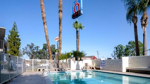 A swimming pool with lounge chairs and palm trees in the background. - Queen Bed | Smoking, Micfridge (Bakersfield)