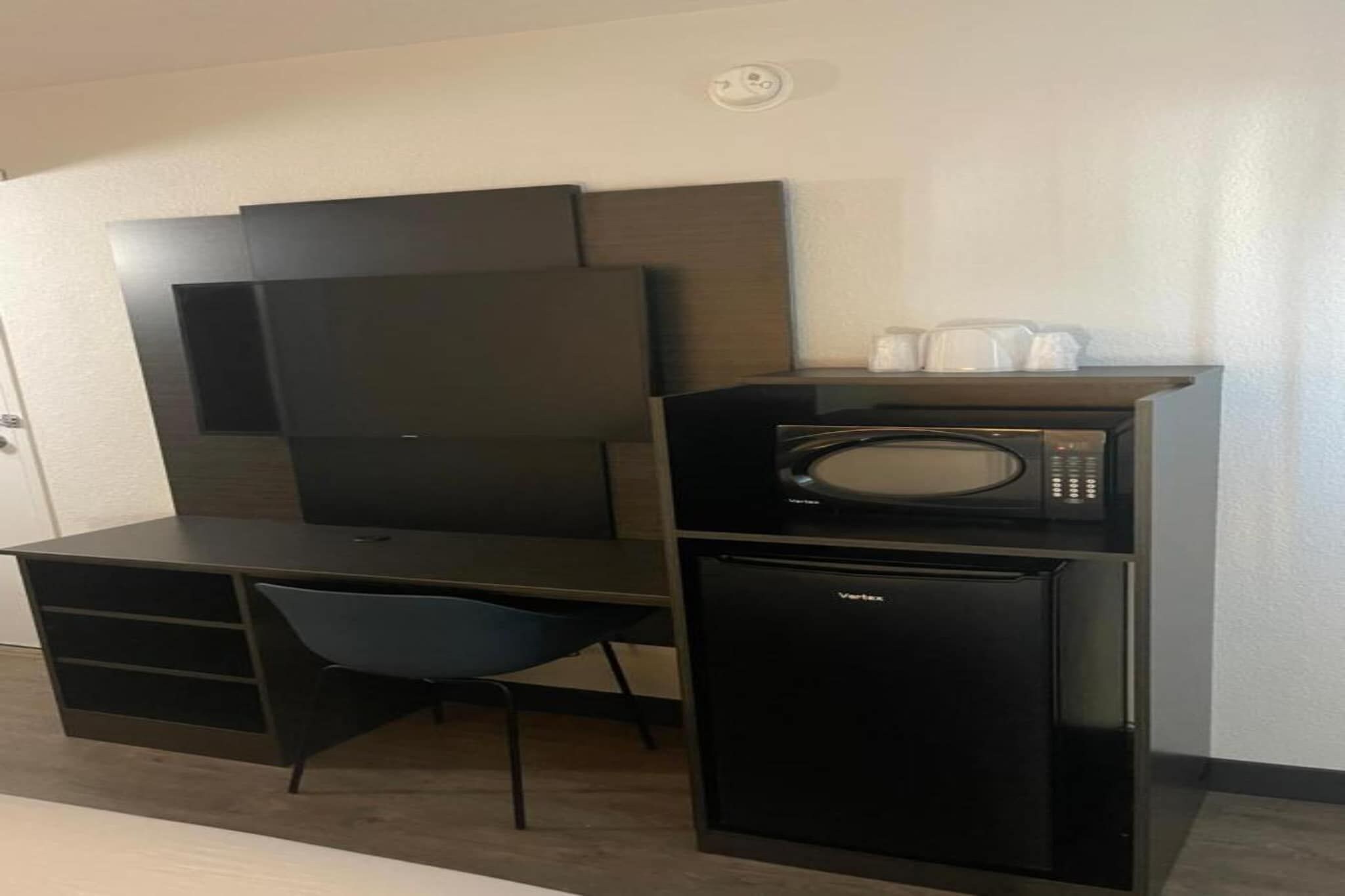 Una kitchenette compacta con microondas, un refrigerador pequeño y una silla.