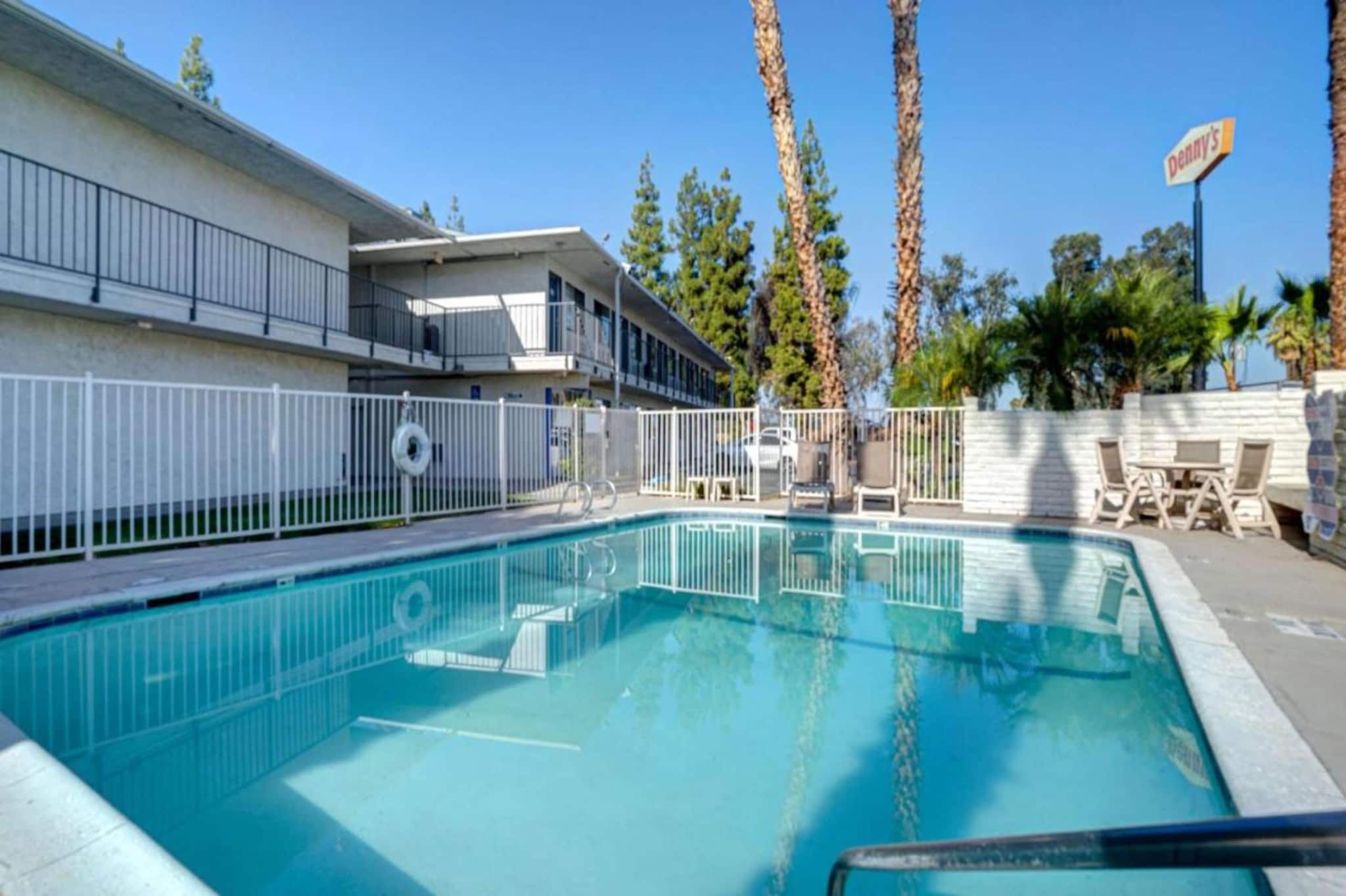 Una piscina con un borde cercado, un edificio con balcón y palmeras al fondo.