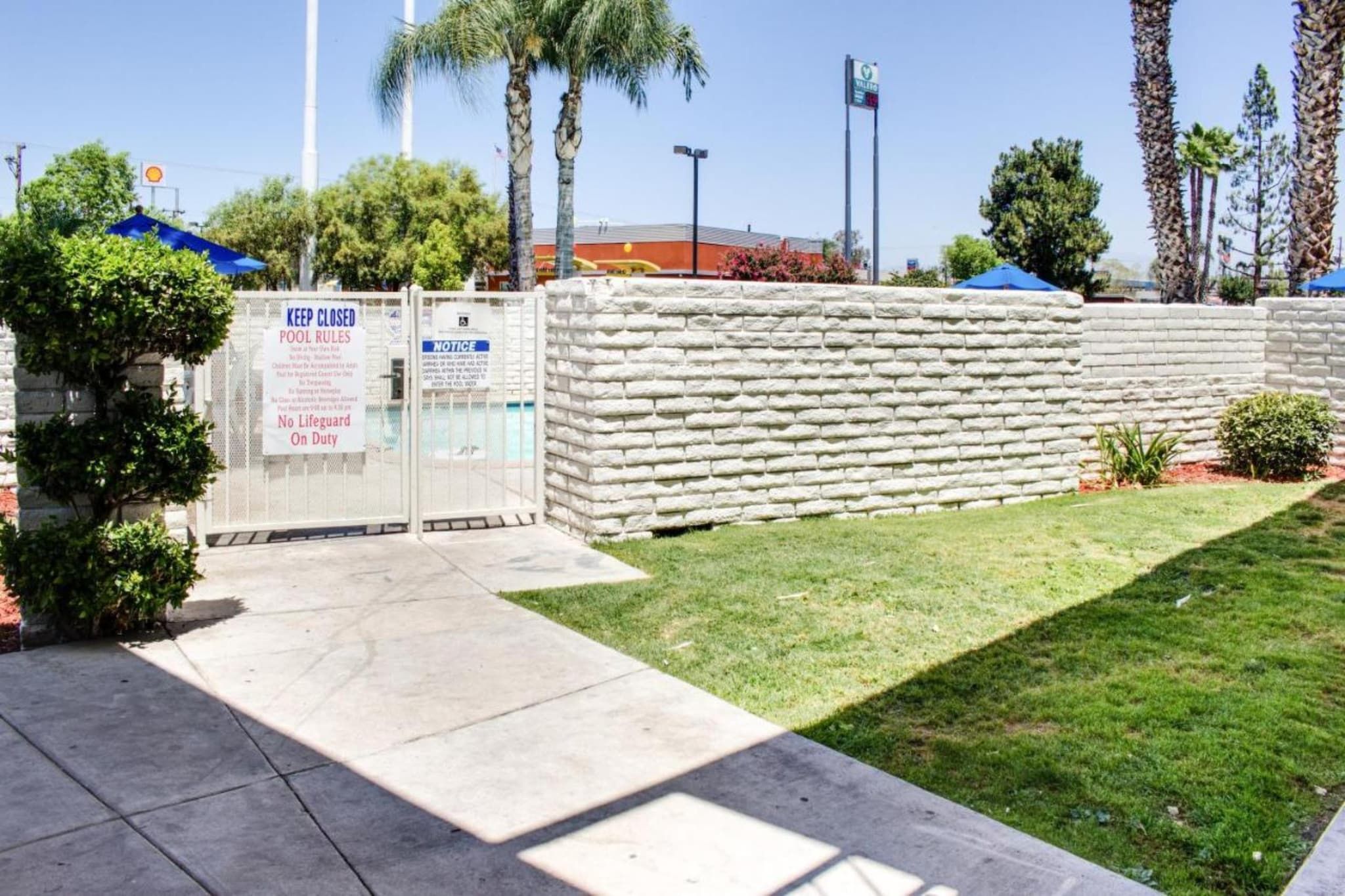 Zona de piscina amurallada con un cartel que indica ausencia de socorrista y normas de la piscina.
