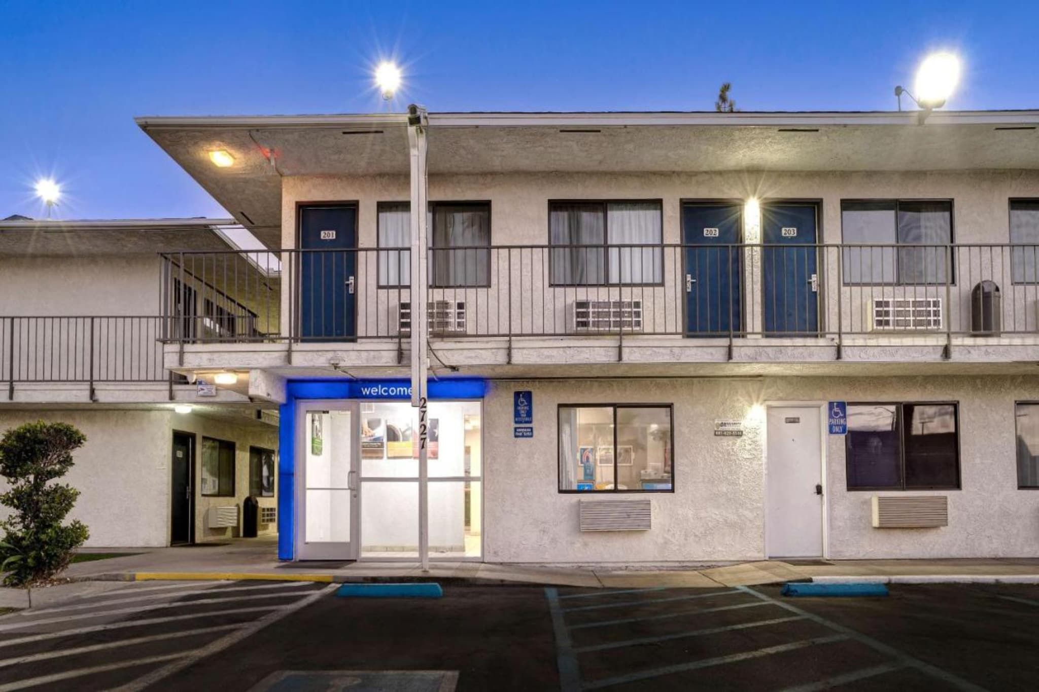 Un motel de dos pisos con entrada azul, habitaciones numeradas y estacionamiento.