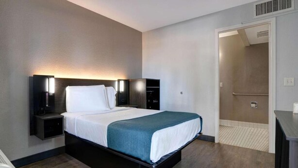 A hotel room with a bed, bedside tables, a wardrobe, and a bathroom door. - Cozy 1 Queen Bed | Smoking (Bakersfield)