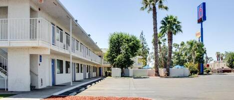 Un motel con estacionamiento, un corredor techado y palmeras.