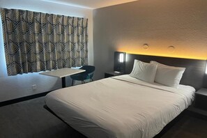 Una habitación de hotel con una cama grande, un escritorio, una silla y una cortina estampada.