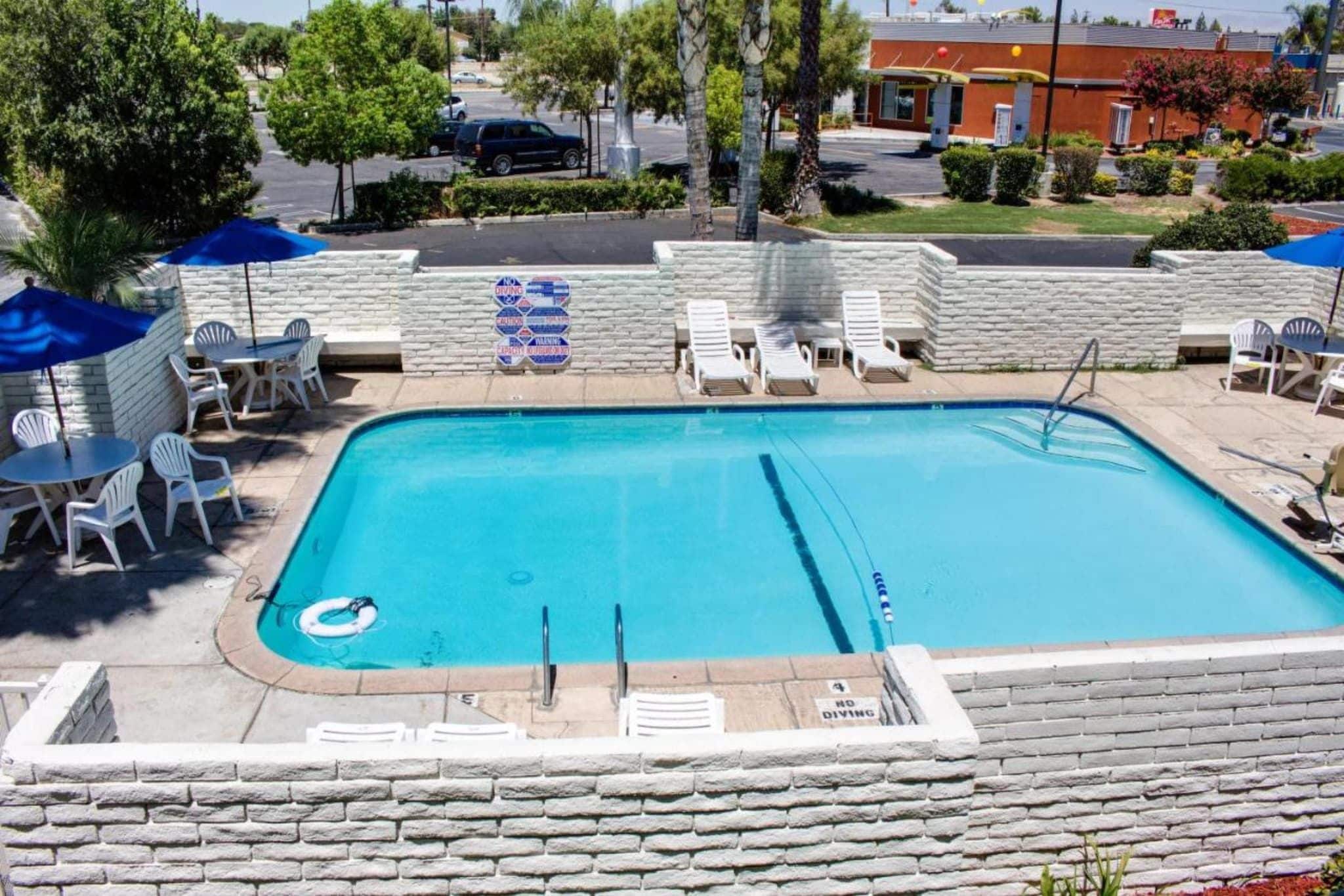A rectangular swimming pool with a diving board, surrounded by white lounge chairs and umbrellas.
