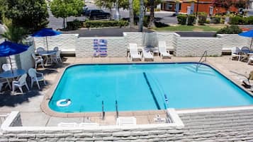 A rectangular swimming pool with a diving board, surrounded by white lounge chairs and umbrellas.