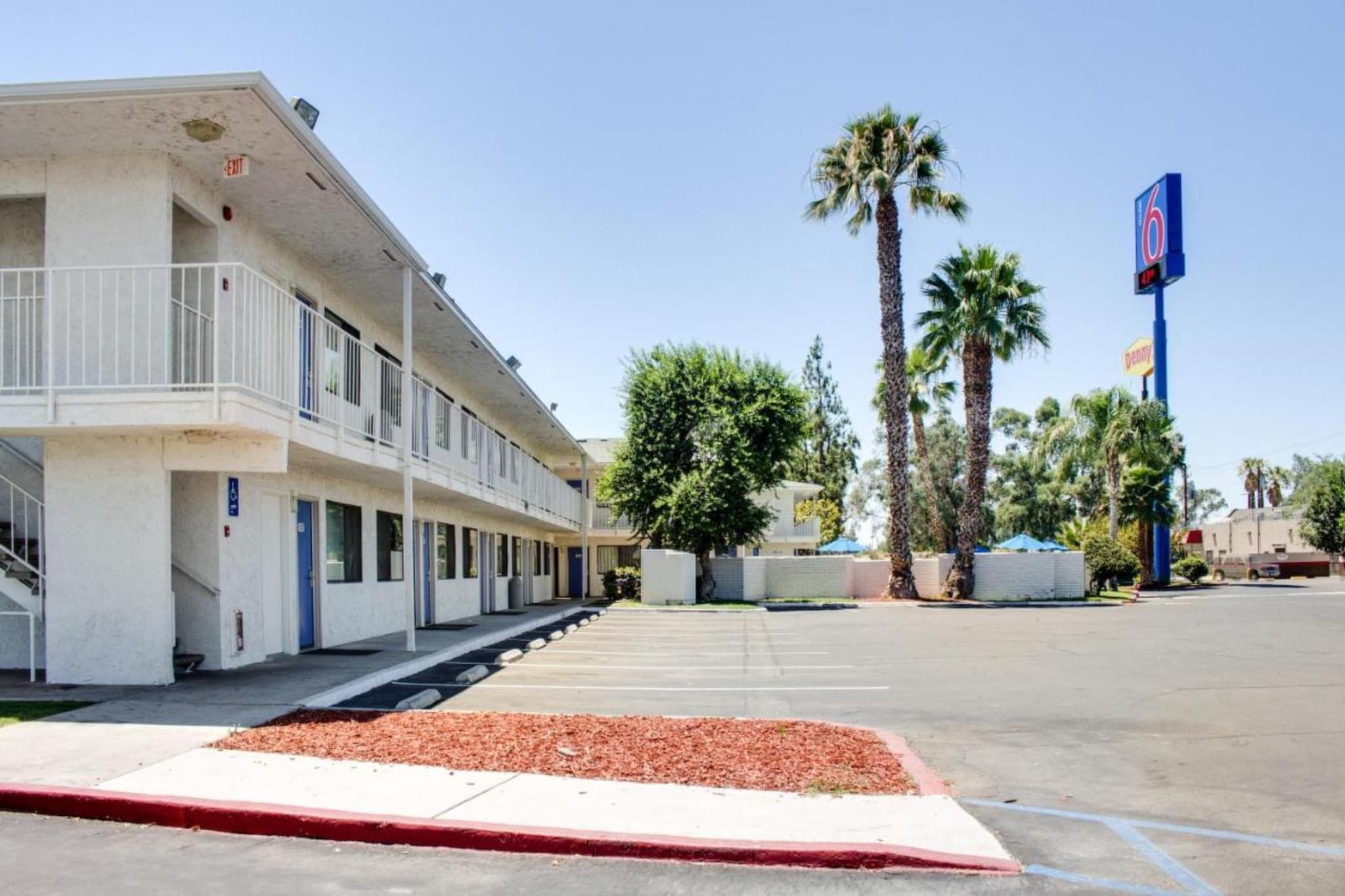 A motel with a parking lot, a covered walkway, and palm trees.