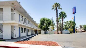 A motel with a parking lot, a covered walkway, and palm trees.