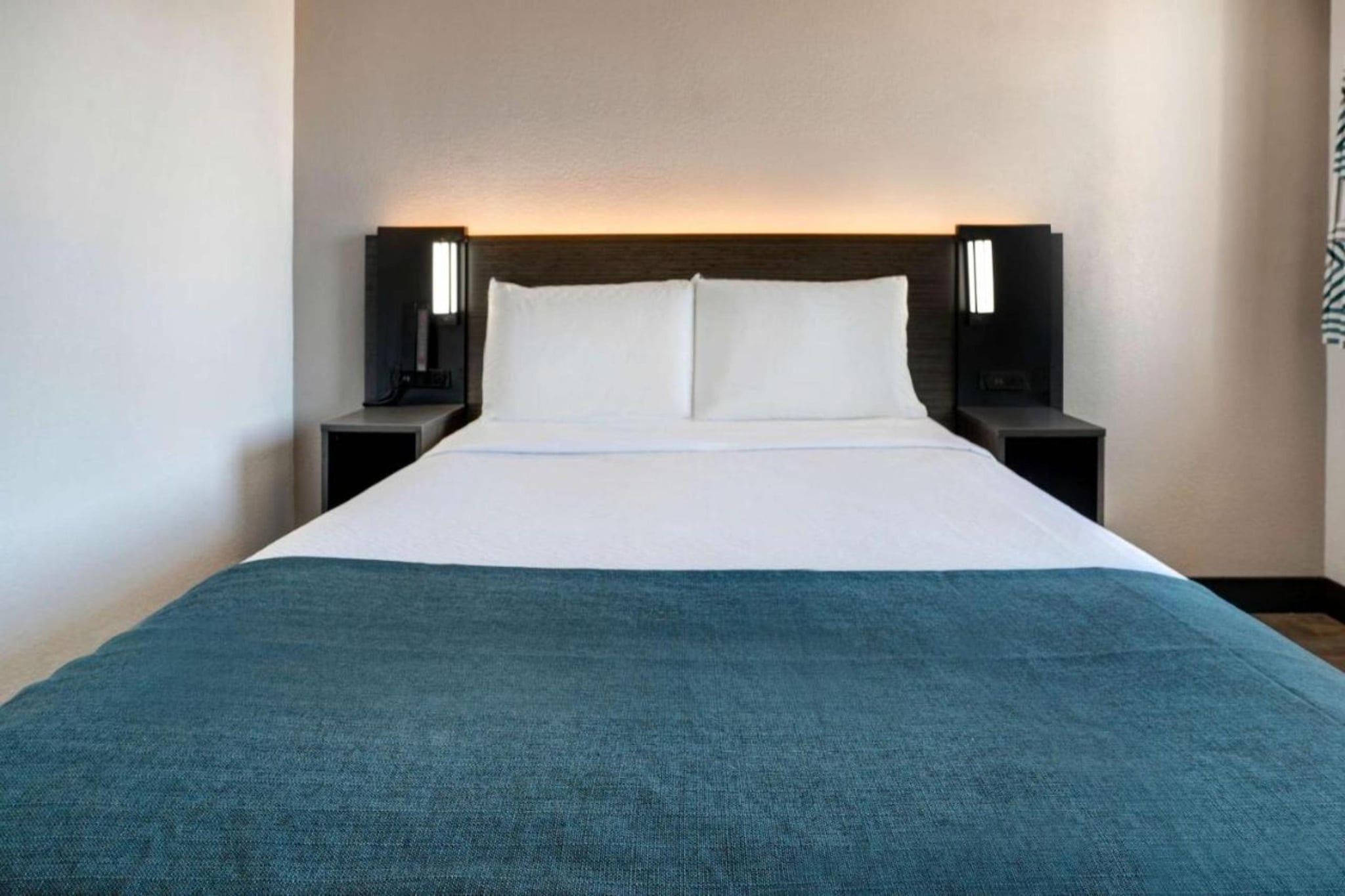 A hotel room with a bed, two bedside tables, and a headboard.
