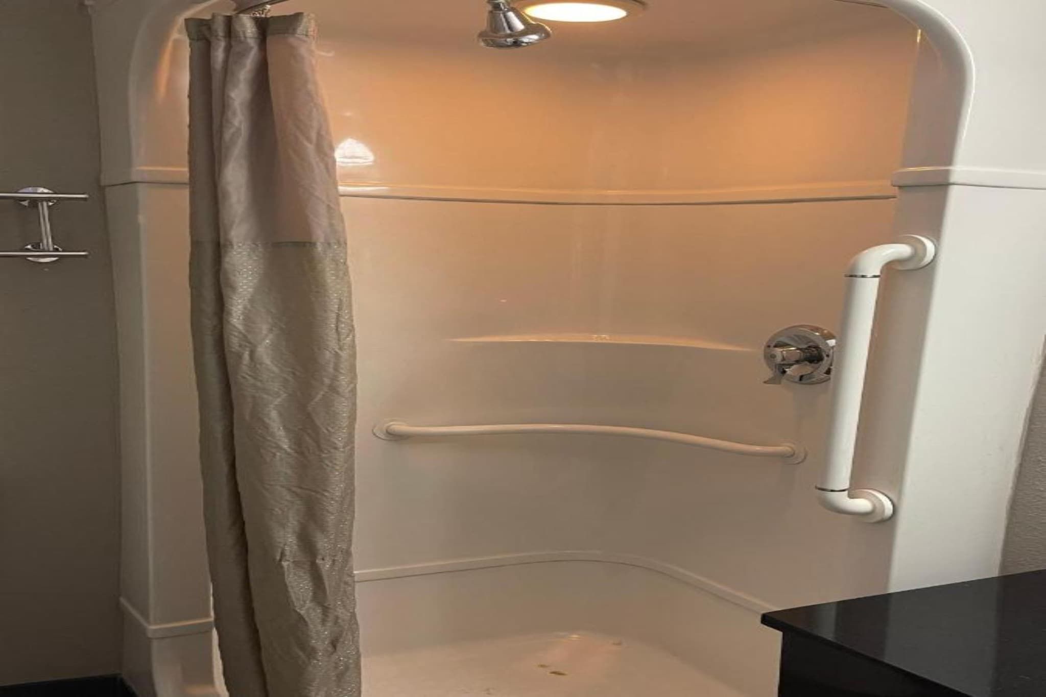 A corner shower with a curved door, a handrail, and a ceiling-mounted light fixture.