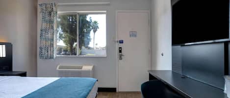 Habitación de hotel con cama, escritorio, televisor de pantalla plana, ventana con vista a palmeras y aire acondicionado.