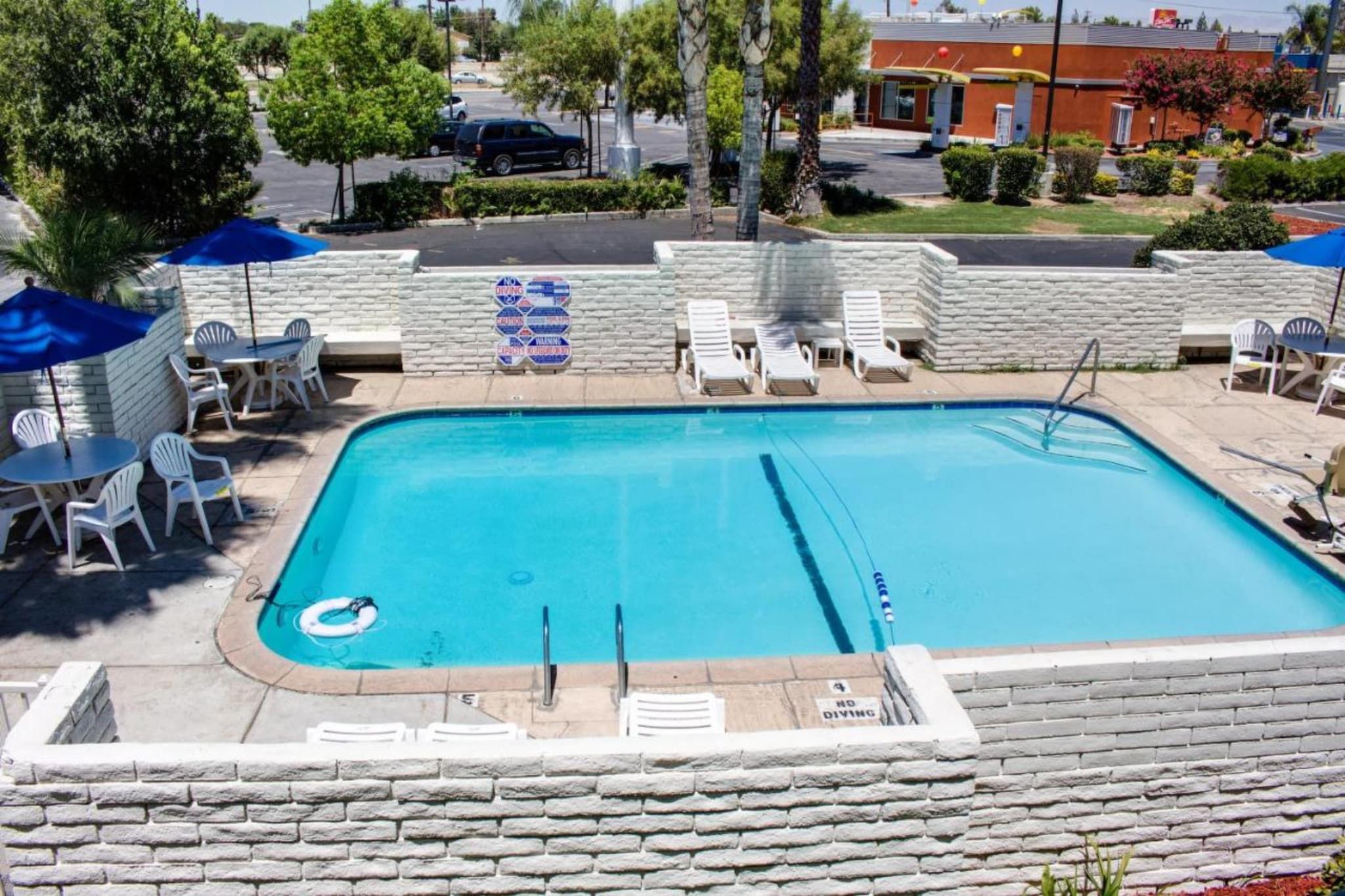 A rectangular swimming pool with a diving board, surrounded by white lounge chairs and umbrellas.