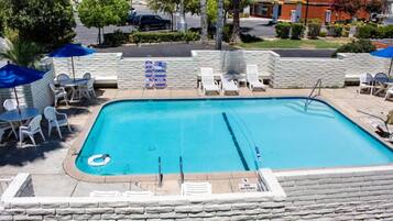 A rectangular swimming pool with a diving board, surrounded by white lounge chairs and umbrellas.