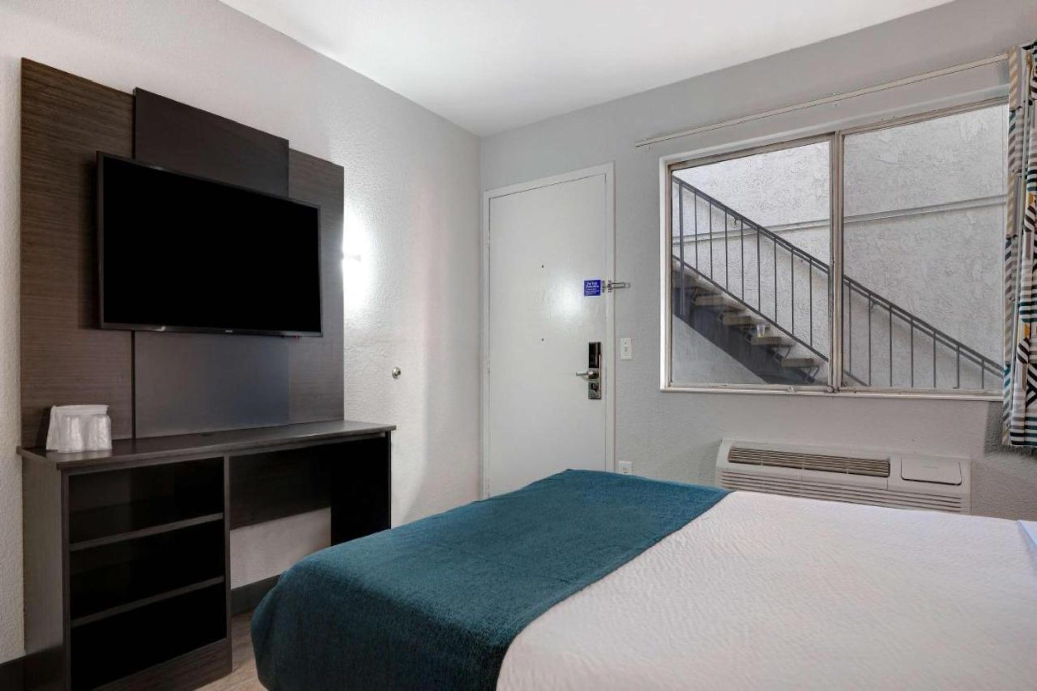 A hotel room with a bed, a TV mounted on the wall, a staircase, and a window.