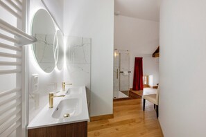 Ein modernes Badezimmer mit Waschbecken in Weiß, goldenen Armaturen, einem großen Spiegel und einer Duschkabine aus Glas.