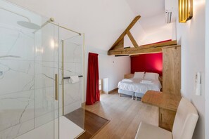 Ein modernes Hotelzimmer mit einer Duschkabine aus Glas, einem Bett mit weißen Leinen und einer roten Akzentwand.