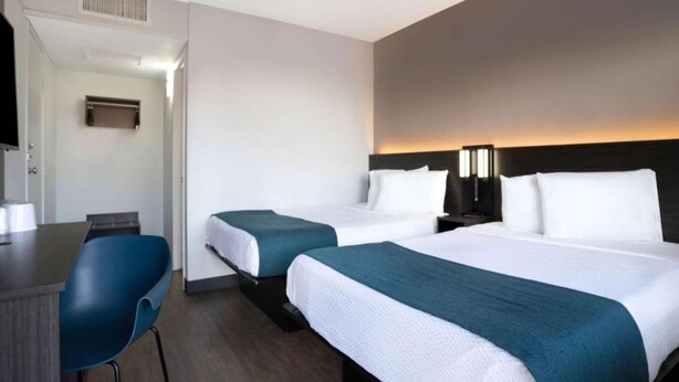 A hotel room with two beds, a desk, and a chair. - Sunny 2 Full Beds | Smoking (Bakersfield)