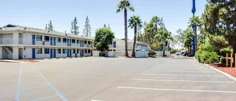 A motel with a parking lot, multiple-story buildings, and palm trees.