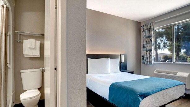 Quarto de hotel moderno com cama, mesa de cabeceira, janela com vista e banheiro com vaso sanitário e porta-toalhas.