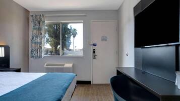 Habitación de hotel con cama, escritorio, televisor de pantalla plana, ventana con vista a palmeras y aire acondicionado.