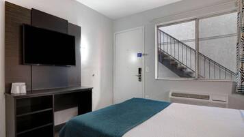 A hotel room with a bed, a TV mounted on the wall, a staircase, and a window.