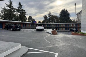Ein Parkplatz mit zwei Autos, ein Gebäude mit der Aufschrift 'St. Luke's' und eine Baumreihe.