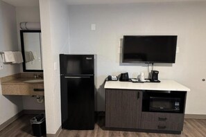 Una kitchenette compacta con refrigerador, microondas, cafetera y televisor de pantalla plana.