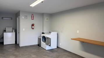 Une buanderie équipée d’un lave-linge, d’un sèche-linge et d’un extincteur fixé au mur.