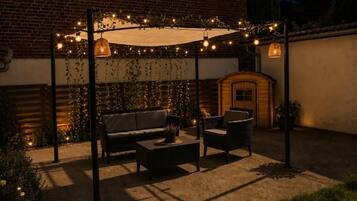 En udendørs patio med en murstensvæg, en trædør og et pergola med lyskæder.