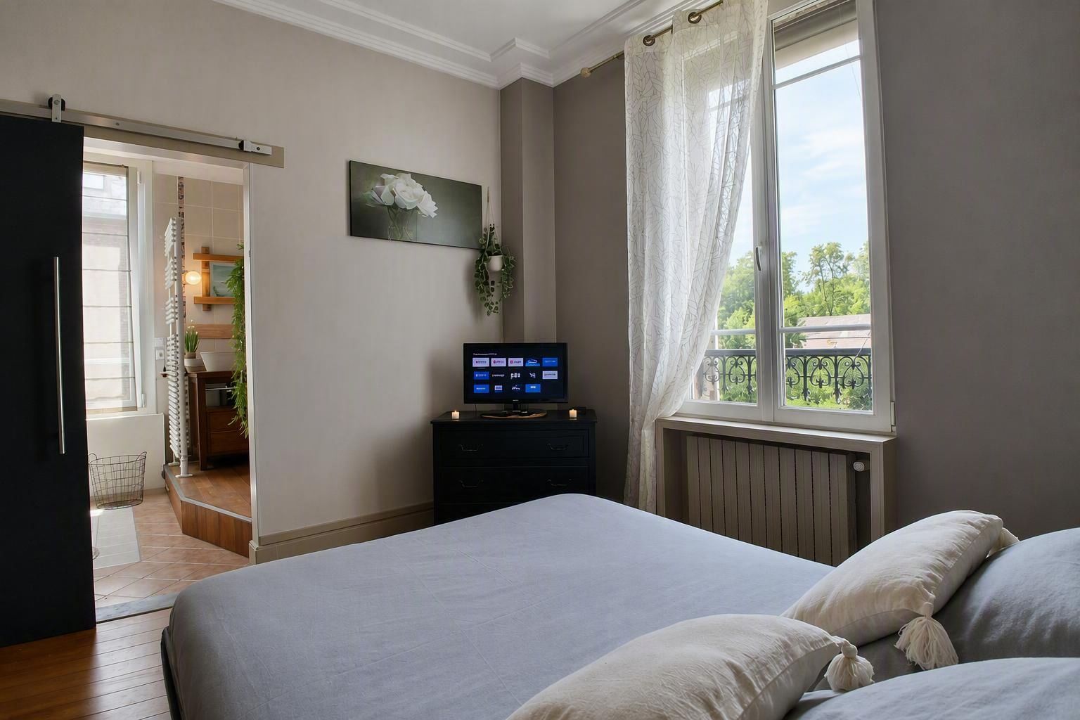 Une chambre à coucher avec un lit, un téléviseur posé sur un meuble, une fenêtre avec des rideaux et une vue sur l’extérieur.