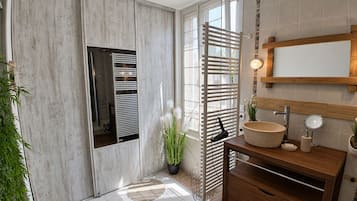 Une salle de bain avec un meuble-lavabo en bois, un porte-serviettes, un miroir et une plante en pot.