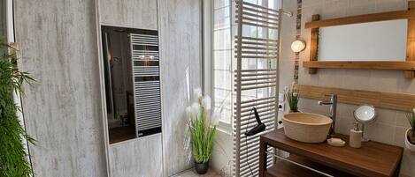 Casa de banho com toucador de madeira, porta-toalhas, espelho e planta em vaso.