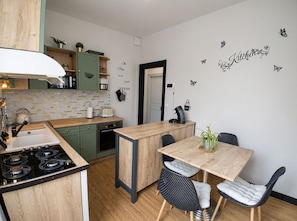 Cocina compacta con una isla central, armarios verdes y un comedor con mesa y sillas.