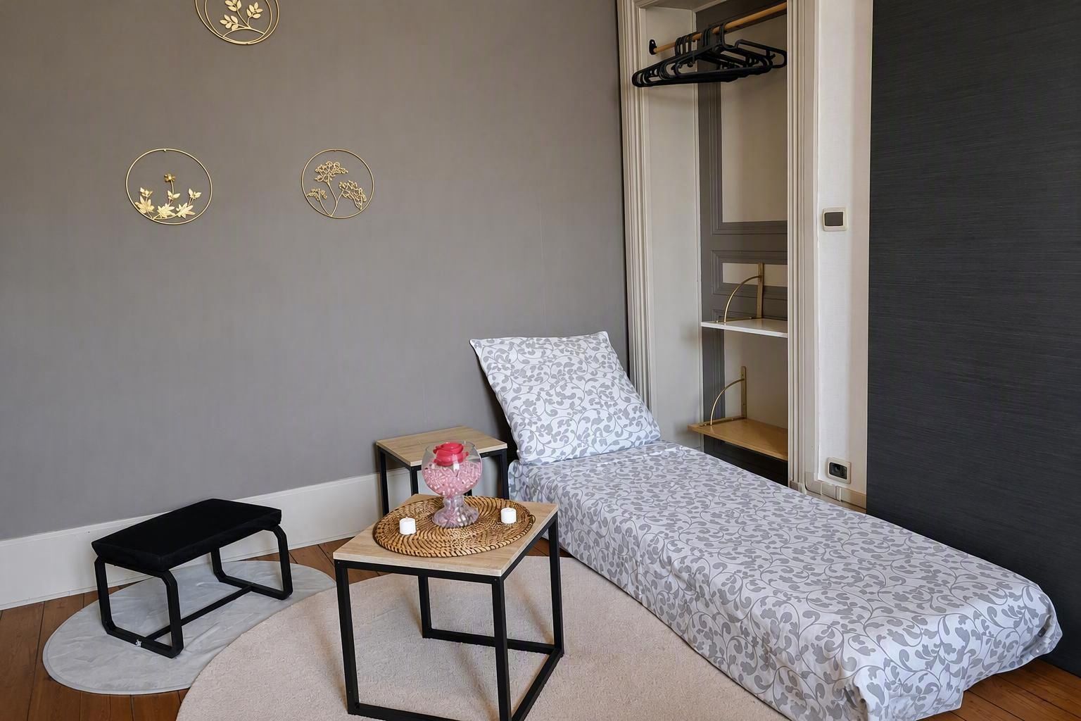 A bedroom with a single bed, a bedside table with a lamp, a small stool, and a wardrobe.