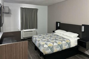 Ein Hotelzimmer mit Bett, Nachttisch, Klimaanlage und einem Vorhangfenster.