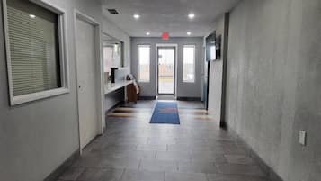Um corredor com piso ladrilhado, um tapete azul e uma porta no final.