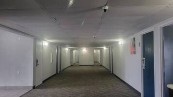 A long, narrow hallway with doors on both sides, a carpeted floor, and a ceiling with recessed lighting.
