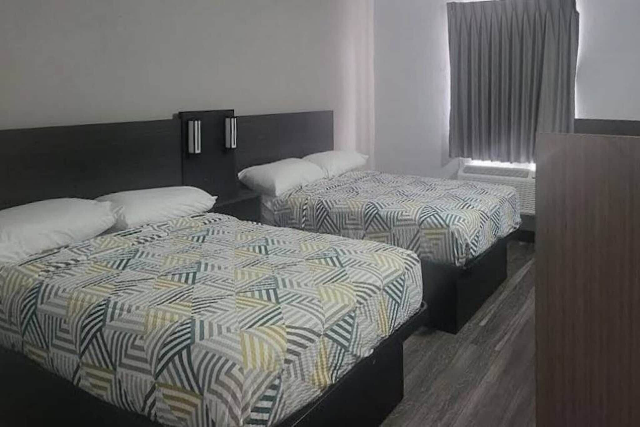 Une chambre d’hôtel avec deux lits, chacun doté d’une literie à motifs, d’une tête de lit sombre et d’une fenêtre avec des rideaux.