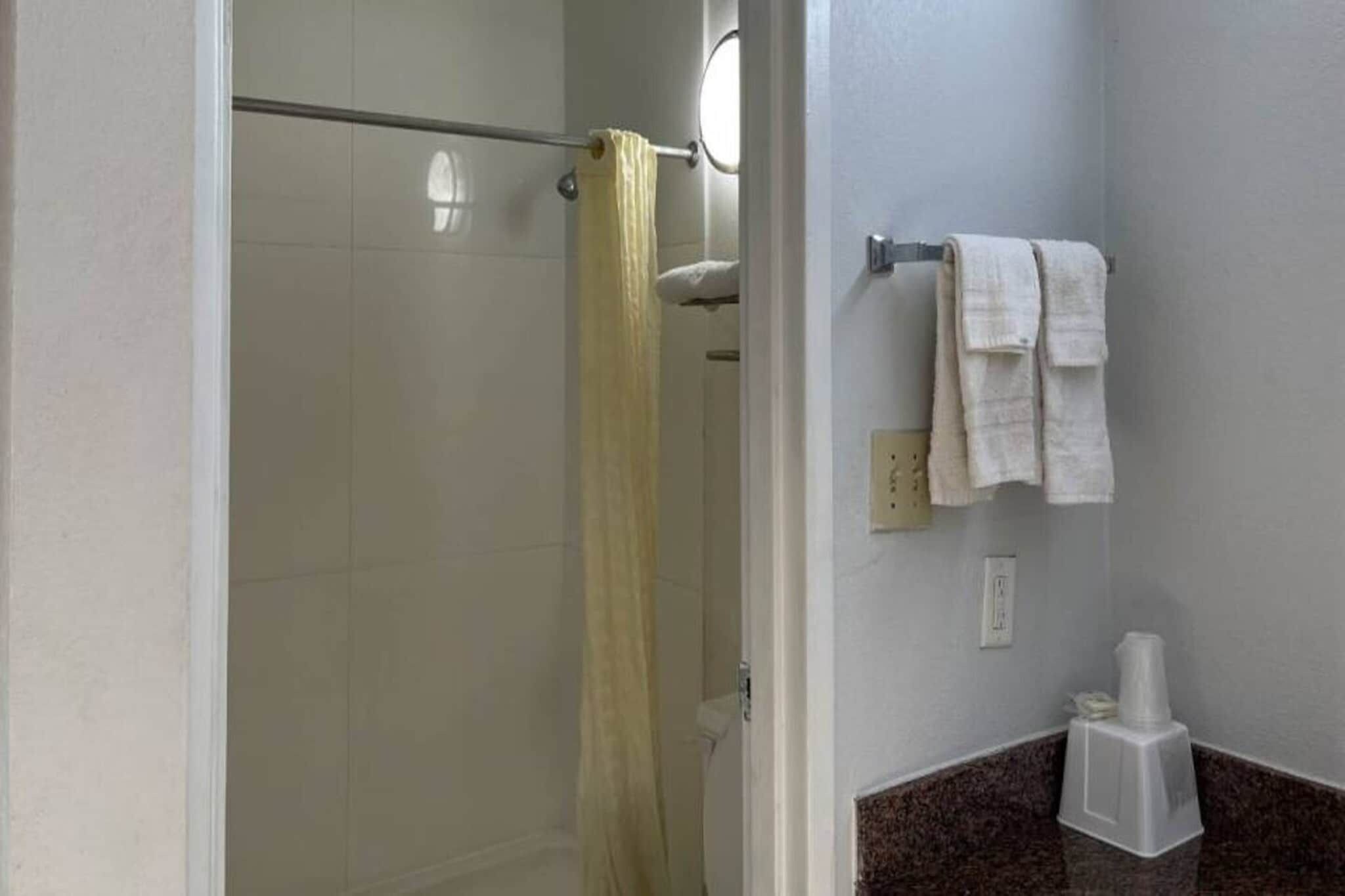 Un baño con ducha, un perchero con toallas y un dispensador de papel higiénico.