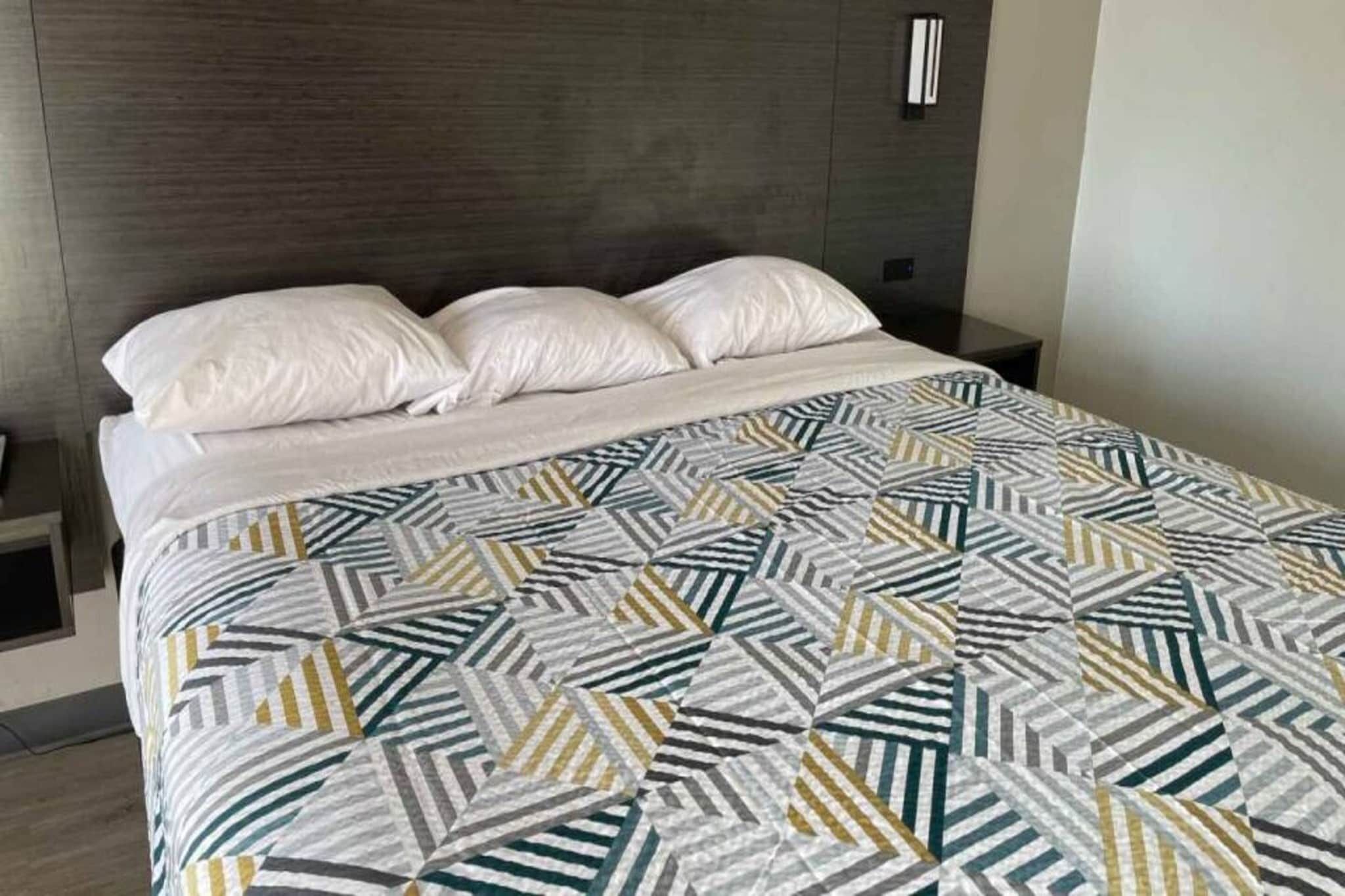 Un letto con una coperta a motivi geometrici, una testiera scura e cuscini bianchi.