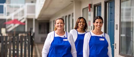 Three individuals in blue aprons standing in front of a building with a blue door and a number '151' sign.