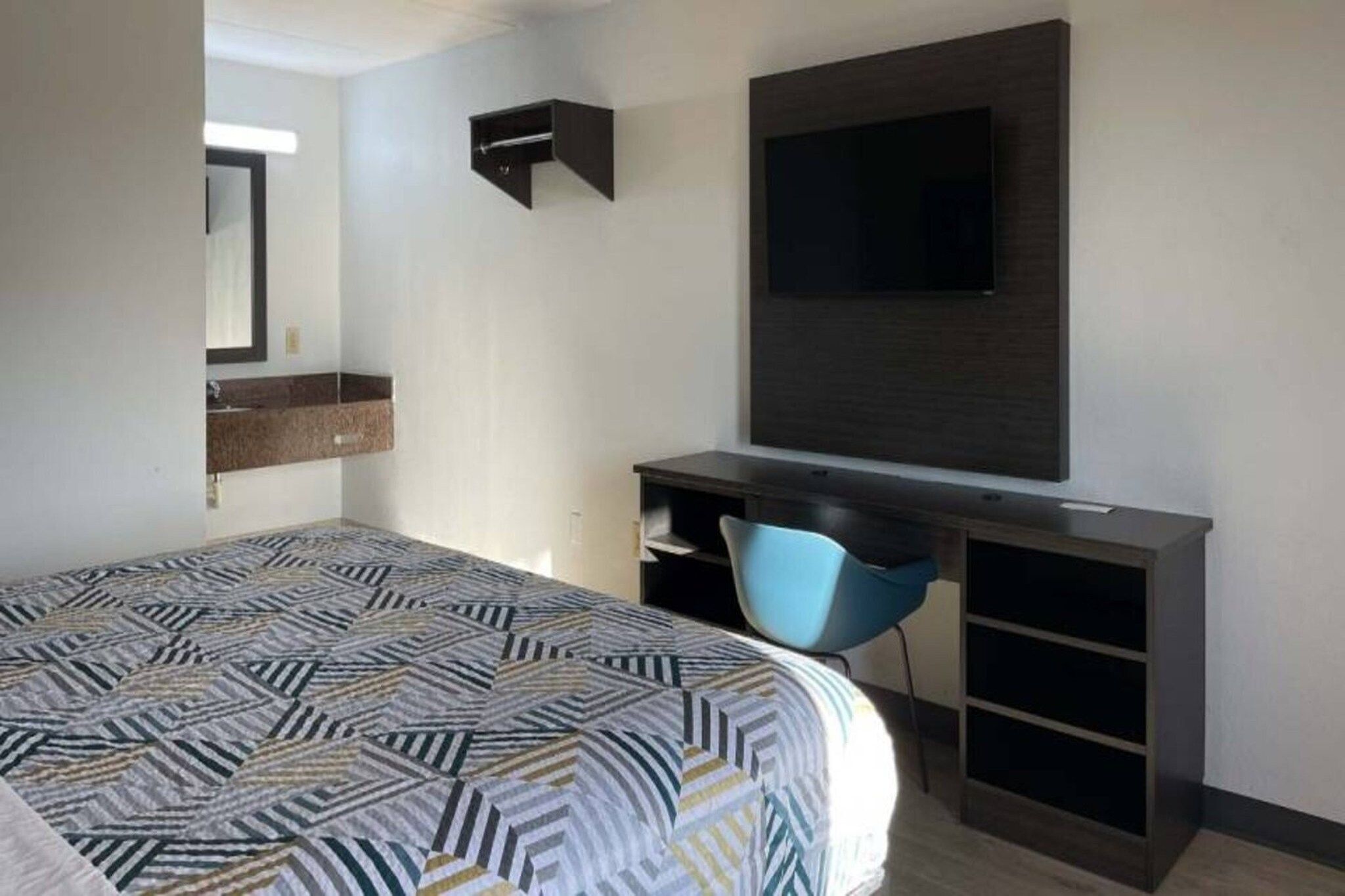 A hotel room with a bed, a desk, a chair, a TV, and a built-in shelf.