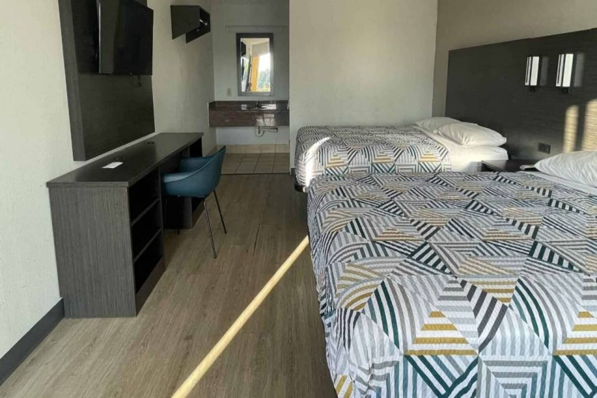 Habitación de hotel con escritorio, dos camas con ropa de cama estampada, un espejo y un televisor.