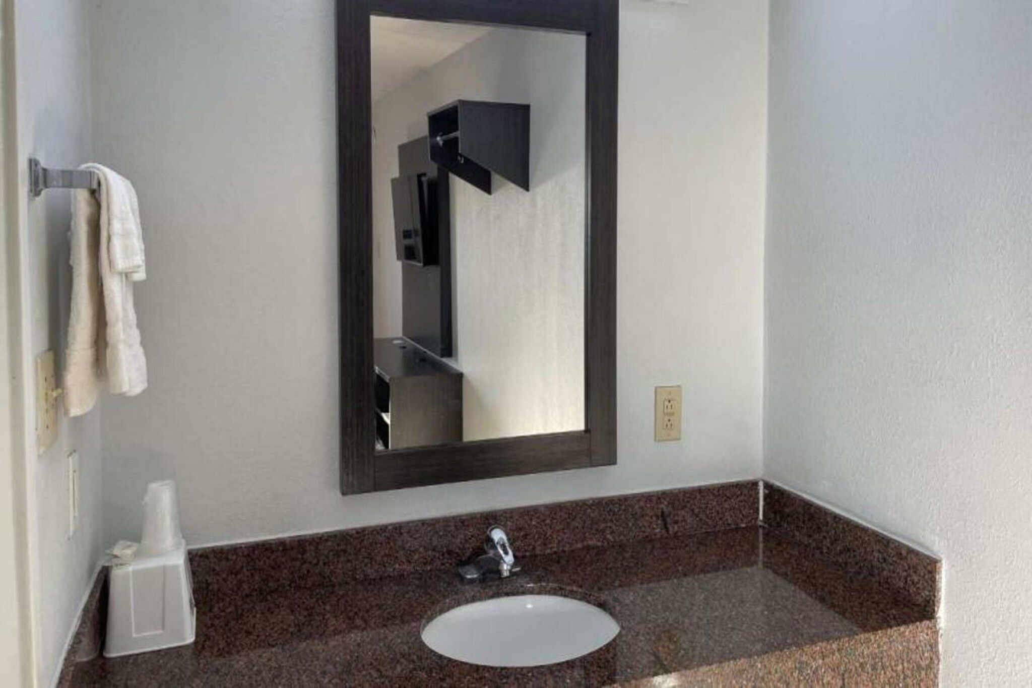Un bagno con lavandino bianco, piano di lavoro in granito scuro, uno specchio e un portasciugamani.